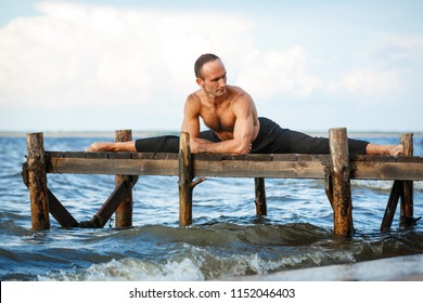 Young yoga trainer practicing split exercises on a wooden pier on a sea or river shore. Healthy lifestyle concept