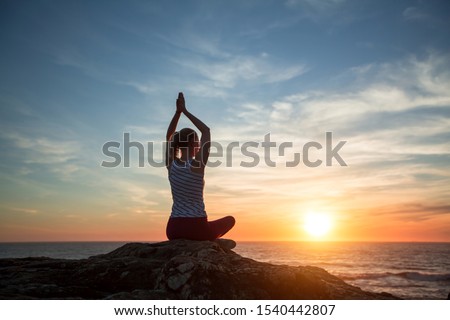 Young yoga woman meditation on the ocean beach at amazing sunset.  