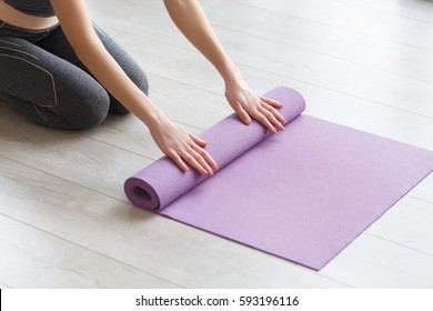 Young yoga Woman rolling her lilac mat after a yoga class on wooden floor near a window, close up - Shutterstock ID 593196116