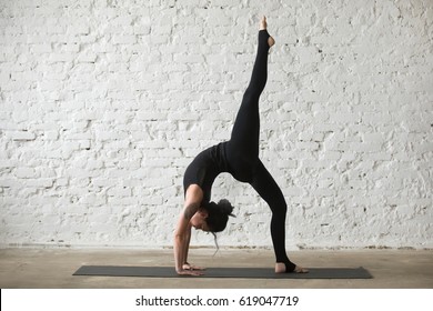 Young yogi attractive woman practicing yoga concept, standing in One legged Wheel exercise, Bridge pose, working out, wearing sportswear, black tank top and pants, full length, white loft background  - Shutterstock ID 619047719