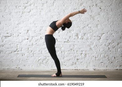 Young yogi attractive woman practicing yoga concept, stretching in Ardha Chakrasana exercise, Standing Backward Bend pose, working out, wearing black sportswear, full length, white loft background  - Shutterstock ID 619049219