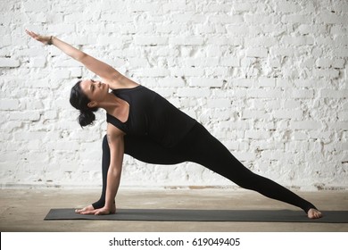 Young yogi attractive woman practicing yoga concept, standing in Utthita parsvakonasana exercise, Extended Side Angle pose, working out, wearing black sportswear, full length, white loft background  - Powered by Shutterstock