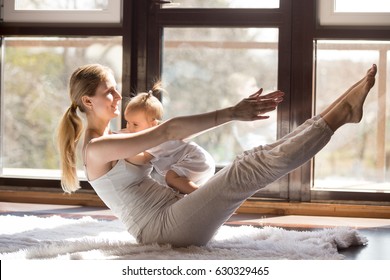 Young yogi happy mother working out, sitting in boat balance pose, wearing white sportswear,  baby on her tummy, fitness at home when having no time for gym, postnatal yoga. Healthy lifestyle concept 