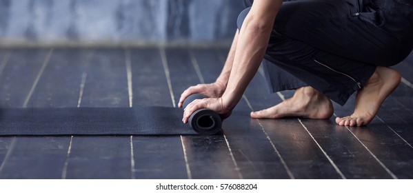 Young yogi men rolling mat after a yoga on black wooden floor. Close up of man hands with black mat, copy space. Healthy Fitness background. Banner and mock up concept