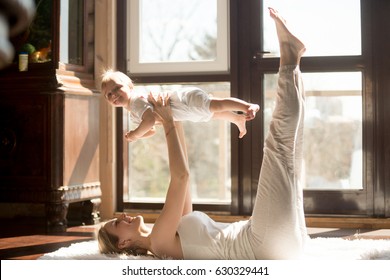 Young yogi smiling mother doing yoga exercise at home, wearing white sportswear, holding high funny daughter, enjoying activities with baby, fun and sport practice. Healthy lifestyle concept photo 