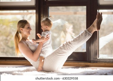 Young yogi smiling mother working out engaging her playful child, toning abs muscles, , integrating baby into yoga practice, fitness at home when having no time for gym. Healthy lifestyle concept 