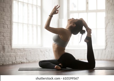 Young Yogi Woman Practicing Yoga Concept, Doing One Legged King Pigeon Exercise, Eka Pada Rajakapotasana Pose, Working Out, Wearing Sportswear Bra And Pants, Silhouette, White Loft Studio Background 