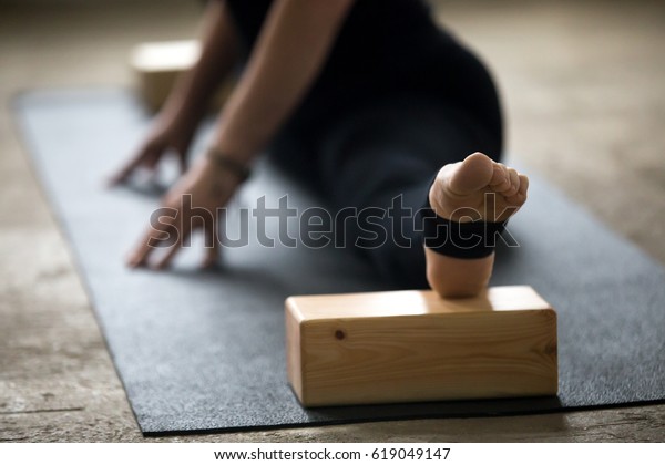 Young yogi woman practicing yoga concept, doing advanced\
splits, Straight Angle exercise, Samakonasana pose using blocks for\
deep stretch, working out on mat wearing black pants, leg close up,\
studio 