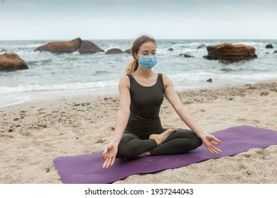 Young yogi woman in sports uniform meditates in a medical mask sitting on mat at beaches. Harmony - Powered by Shutterstock