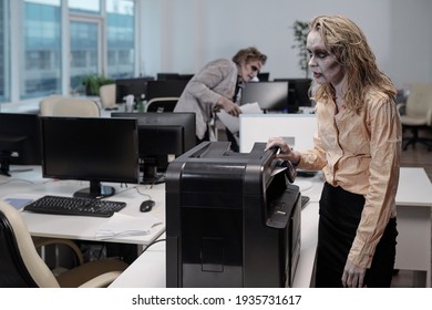 Young zombie businesswoman standing by xerox machine while making copies of documents