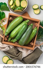 Young zucchini in a wooden box on a gray background. Top view, vertical.