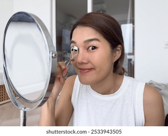 Young-adult Asian Thai woman wearing makeup, using eyelash curler, morning routine beauty concept. High quality photo - Powered by Shutterstock