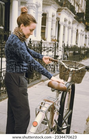 Young-adult woman picking her pink bicycle with a basket and a bell parked on the street of the city. Urban non-motorized vehicle with no carbon emissions. Healthy lifestyle. Transport. Vertical.