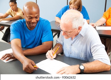 Younger College Student Tutors Mature Older Student Who Is Struggling To Keep Up.  Focus On The Tutor.