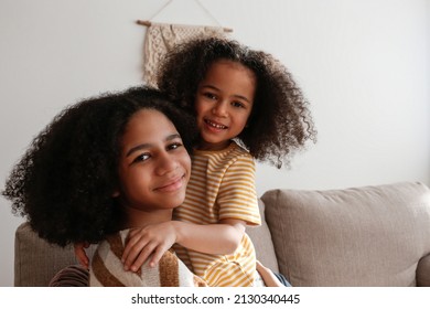 Younger and older sister spending time together at home. Two black girls of different age hugging and showing affection. Black female siblings having fun and bonding. Background, copy space, close up. - Shutterstock ID 2130340445