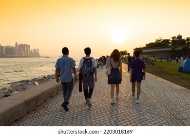 Youngsters Students Boy And Girl Chat And Walk During Sunset In West Kowloon Waterfront Promenade, Hong Kong In Evening. Back Light Shot