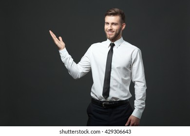 Your Logo Or Product Goes Here! Studio Shot Of Handsome Young Businessman Holding His Arm Up Presenting Copyspace.