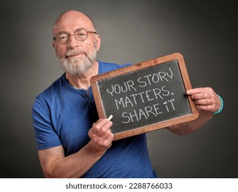your story matters, share it - white chalk writing on a retro blackboard held by a senior man, presenter, teacher or mentor
