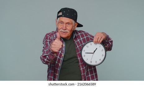 It Is Your Time. Portrait Of Senior Man In Shirt Showing Time On Clock Watch, Ok, Thumb Up, Approve, Pointing Finger At Camera. Mature Grandfather Indoors Studio Shot Isolated Alone On Gray Background