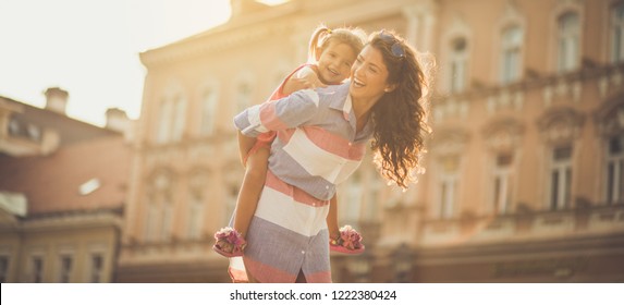 You're Always Safe On Your Mother's Back. Single Mother With Her Daughter In City. Carrying On Piggyback. Close Up. Copy Space.