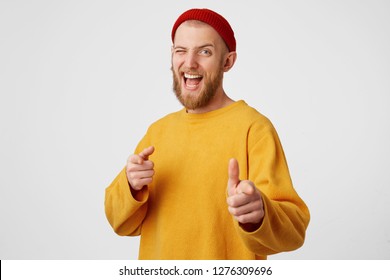 You're chosen bro. A young attractive interesting unusual guy dressed in a yellow sweater and a red hat winks with one eye, his finger points to the camera, encouraging, an approving gesture. - Shutterstock ID 1276309696
