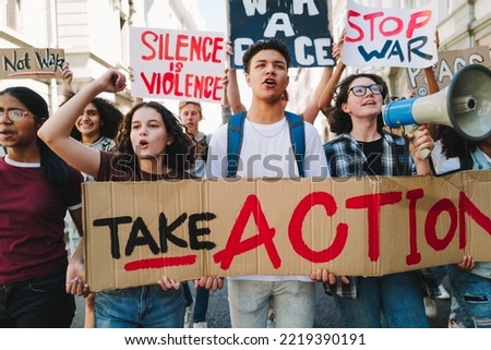 Youth activism for peace and human rights. Group of multicultural peace activists marching the streets with posters and banners. Diverse young people protesting against war and violence.
