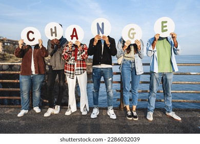 Youth Advocating for Change: Multiracial young people cover faces with "CHANGE" discs by a railing, sea, and rocks, symbolizing a call for societal transformation - Powered by Shutterstock