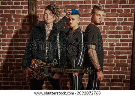 Youth alternative culture. Cool group of punk rock musicians with stylish mohawks posing in black concert costumes against a brick wall. Grunge style. 