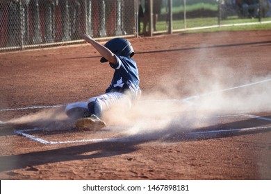 Youth Baseball Player Sliding Into Home Plate With Dust Cloud In Sunlight