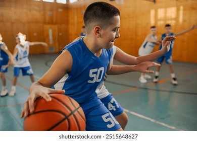 Youth in blue jersey makes a strategic move in a basketball game, with blurred teammates in the background, signifying competition and sport - Powered by Shutterstock