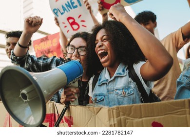 Youth climate activists shouting on a megaphone while marching against climate change. Young people protesting against global warming and pollution. Teenagers joining the global climate strike. - Powered by Shutterstock