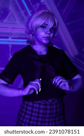 youth cosplay culture, woman in blonde wig and school uniform looking at camera in blue neon light