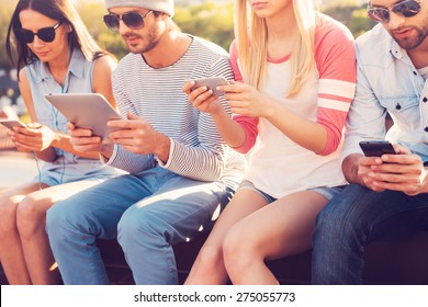 Youth Culture. Four Young People Sitting Close To Each Other And Looking At Their Gadgets