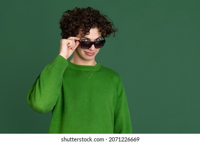 Youth Culture. Portrait Of Young Man In Green Sweater In Stylish Sunglasses Isolated Over Dark Green Background. Concept Of Feelings, Youth, Fashion, Facial Expression, Emotions, Lifestyle, Ad