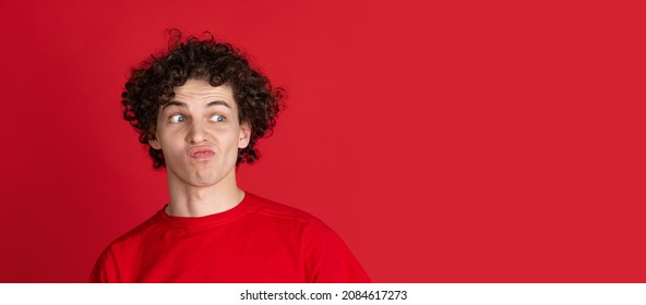 Youth Culture. Portrait Of Young Man In Casual Cloth Making Faces Isolated Over Red Background. Concept Of Feelings, Youth, Fashion, Facial Expression, Emotions, Lifestyle, Ad