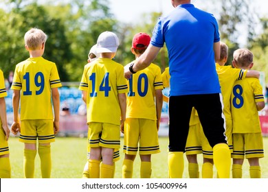 Youth Football Coach Talking To Childrens Soccer Team. Young Football Players With Coach. Soccer Coach Coaching From The Bench. 