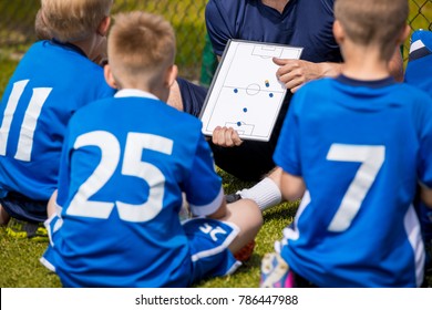 Youth Football Team With Coach At The Soccer Stadium. Boys Listening To Coach's Instructions Before Competition. Coach Giving Team Talk Using Soccer Tactics Board