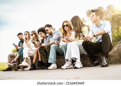 Youth Friends Community Phubbing Using Smartphones Sitting Outdoors On A Bench - Lifestyle People And Technology Concept - Filtered Image - Low Angle View