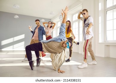 Youth generation. Male hip-hop dancer in motion shows break dance against backdrop of dance group in dance studio. Dancers in bright stylish casual clothes and colored glasses have fun together. - Powered by Shutterstock