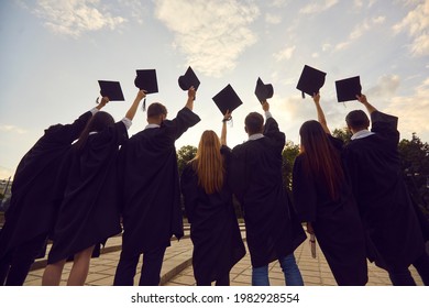 Youth having high hopes. Back view of group of university graduates standing in row holding up black academic caps. Confident college students together tossing hats in air at graduation party
