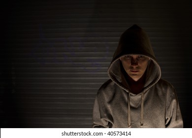 Youth in hooded top in front of garage door with graffiti.