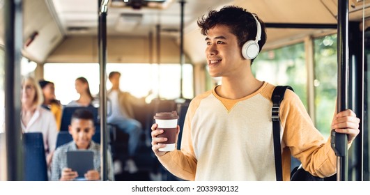 Youth Lifestyle. Positive asian guy standing in public transportation, wearing headphones holding takeout cup and handle, drinking coffee, riding to university looking out of window, banner, panorama - Powered by Shutterstock