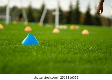 A youth soccer coach conducts a training session on a lush green grass field. Brightly colored cones are set up to guide players during drills under a clear sky - Powered by Shutterstock