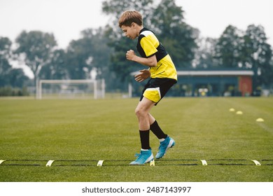 Youth soccer player skipping on training ladder. Young boy running fast and exercising using training equipment. Football player improving speed on training pitch - Powered by Shutterstock