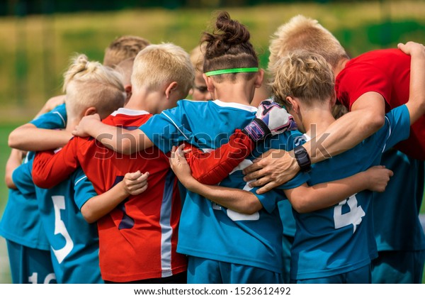 Youth sports coach witch children on soccer field.\
Kids huddling before the final tournament match. Kids bending down\
in huddle