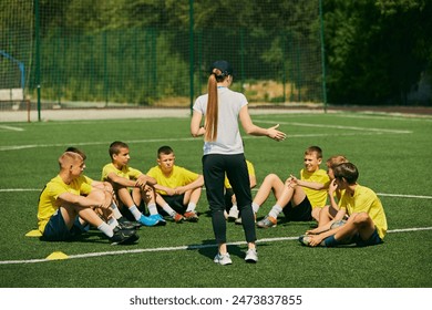 Youth Sports Education. Group of enthusiastic young soccer players listening to strategic advice from female coach, focusing on teamwork and skill development. Sport, school, active lifestyle concept - Powered by Shutterstock