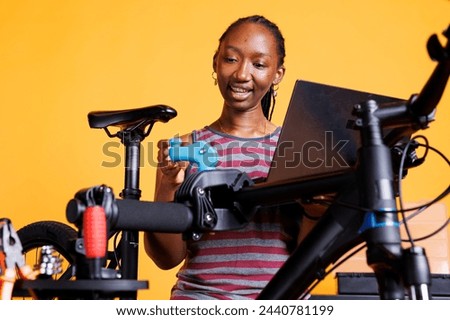 Youthful black woman thoroughly inspecting and repairing damaged bicycle with instructions from laptop. Healthy african american female researching on internet for bike gear maintenance.