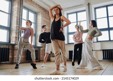 Youthful female performer with arm raised over head standing in front of dance group learning new movements of vogue dancing