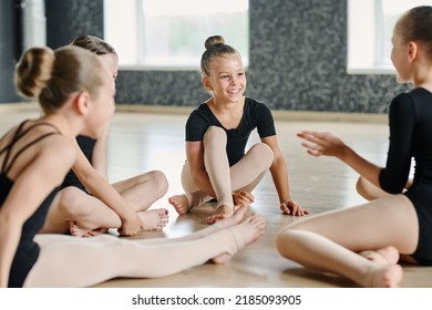 Youthful girls in choreography attire sitting on the floor of classroom or dancing hall and discussing funny stuff after lesson or repetition