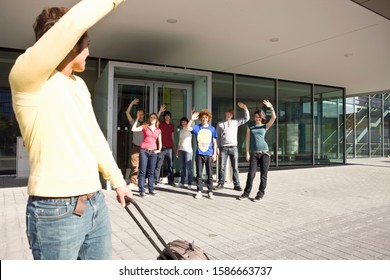 Youthful Group Waving Goodbye To Young Man With Suitcase In Munich, Bavaria, Germany